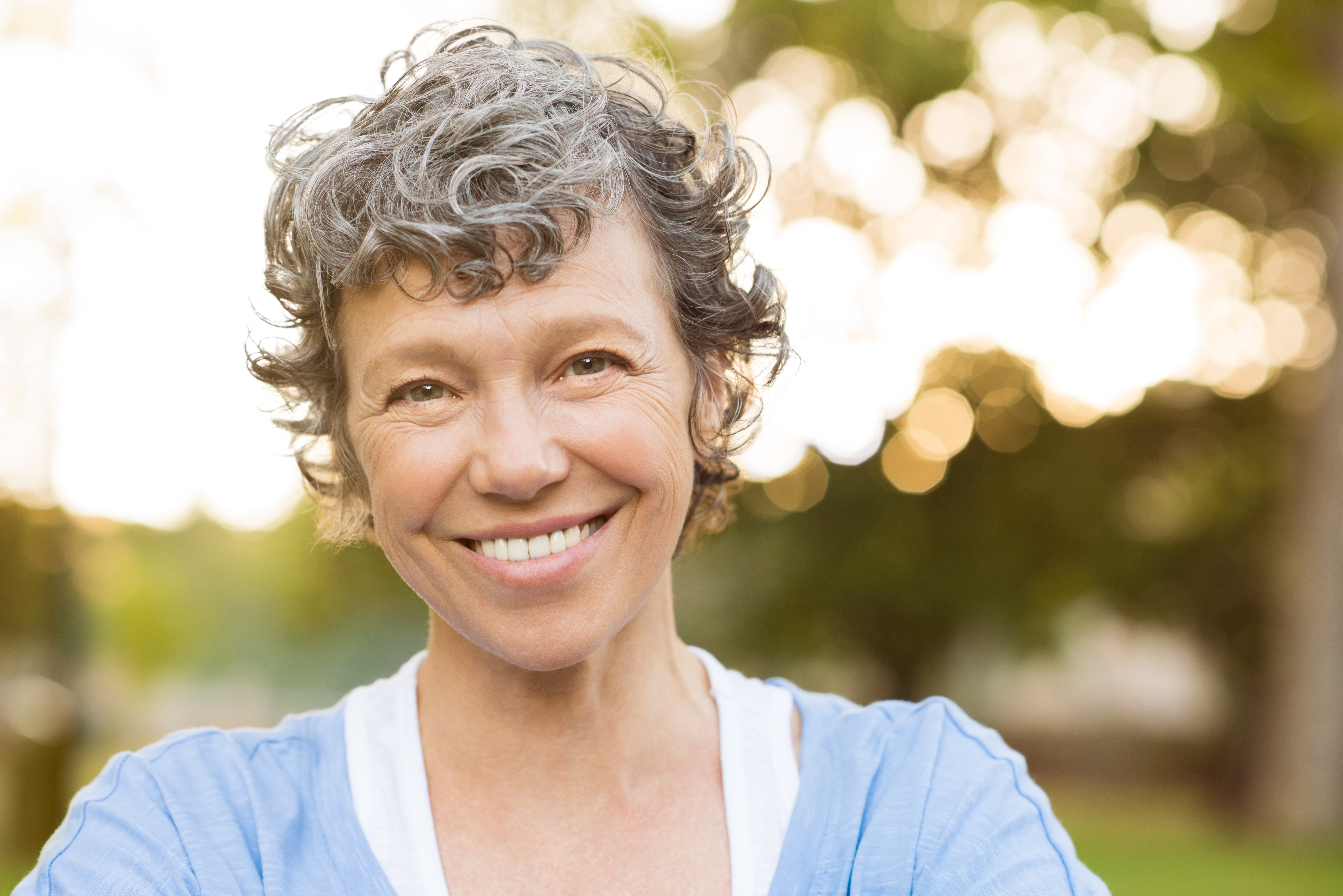 Portrait of senior woman relaxing at park. Close up face of happy senior woman looking at camera. Portrait of a smiling mature woman with grey hair.